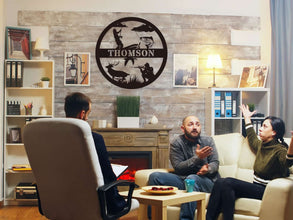 Custom round black metal hunting and fishing sign featuring a fisherman, deer, hunter silhouette, and personalized family name – laser-cut from powder-coated steel for outdoor wall decor.