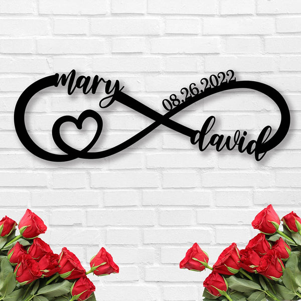 Personalized infinity heart metal sign with custom names and date, laser-cut from black powder-coated steel, displayed against a white brick wall.