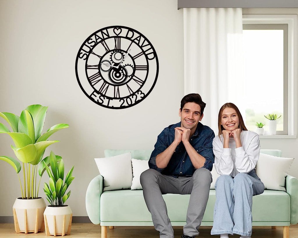 Large personalized black metal wall clock with laser-cut cutout gears, couple names Jason and Laura, center heart icon, established 2023, and Roman numerals.