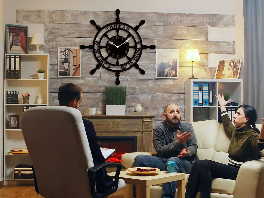 Large personalized black metal wall clock shaped like a ships wheel, featuring laser-cut cutout name Thomas, custom GPS coordinates, and Arabic numbers.