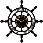 Large personalized black metal wall clock shaped like a ships wheel, featuring laser-cut cutout name Thomas, custom GPS coordinates, and Arabic numbers.
