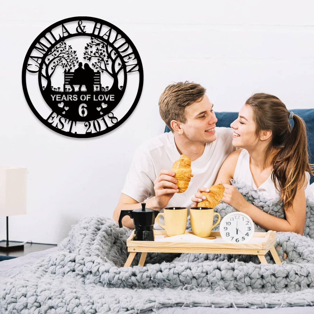 Custom laser-cut steel anniversary sign featuring a couple on a bench with trees, personalized with names, anniversary year, and established date