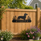 Personalized Dachshund metal dog sign attached to a wooden backyard fence surrounded by flowers and green grass.