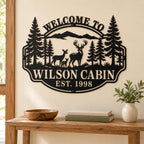 Personalized deer cabin metal sign on a cream wall above a wooden console table with books and a ceramic vase.