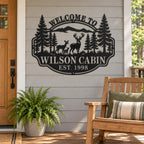 Black deer cabin metal sign on a light gray porch wall beside a wooden chair and potted fern.