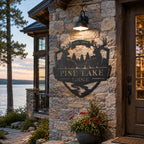 Personalized deer metal lodge sign displayed on a stone wall beside a luxury lake house.