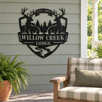 Black deer lodge metal sign on a covered porch beside a wooden chair with plaid cushions.