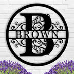 Black circular metal monogram sign with custom family name and botanical patterns.