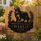 Black personalized dog memorial metal sign mounted on a wooden garden fence in a backyard setting.