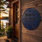 Custom metal lake house sign mounted on a rustic lakeside cabin with family name and crossed paddle design.
