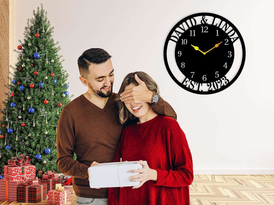 Large personalized black metal wall clock with a solid center dial, featuring laser-cut cutout family names, established 2023, and modern Arabic numbers.