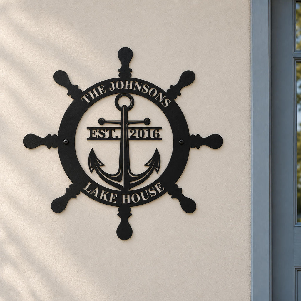 Personalized ship wheel and anchor metal sign mounted on a light wall beside a blue-gray lake house entrance door.