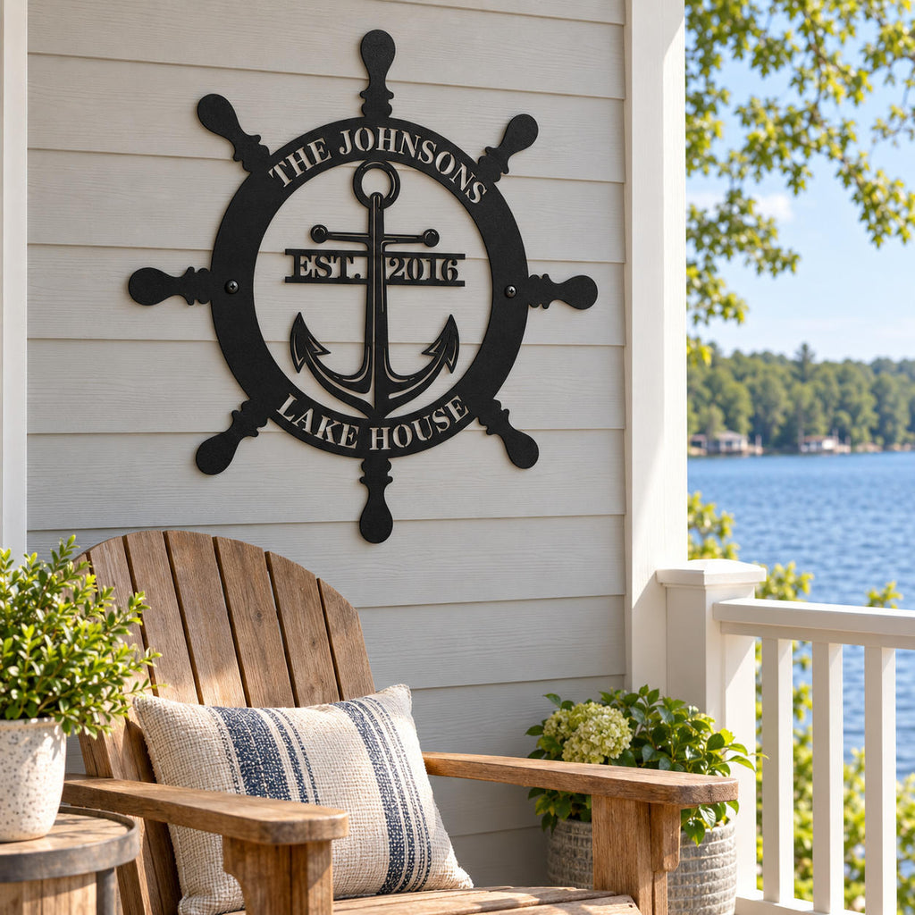 Black nautical metal sign above a wooden porch chair, with a blue lake visible beyond the white railing.