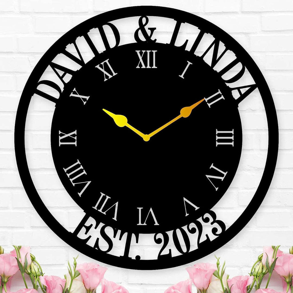 Large personalized black metal wall clock with a solid center dial, featuring laser-cut cutout names David and Linda, established 2023, and Roman numerals showing white wall background.