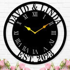 Large personalized black metal wall clock with a solid center dial, featuring laser-cut cutout names David and Linda, established 2023, and Roman numerals showing white wall background.