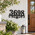 Custom black metal house number sign with decorative scrollwork mounted beside a modern front door.
