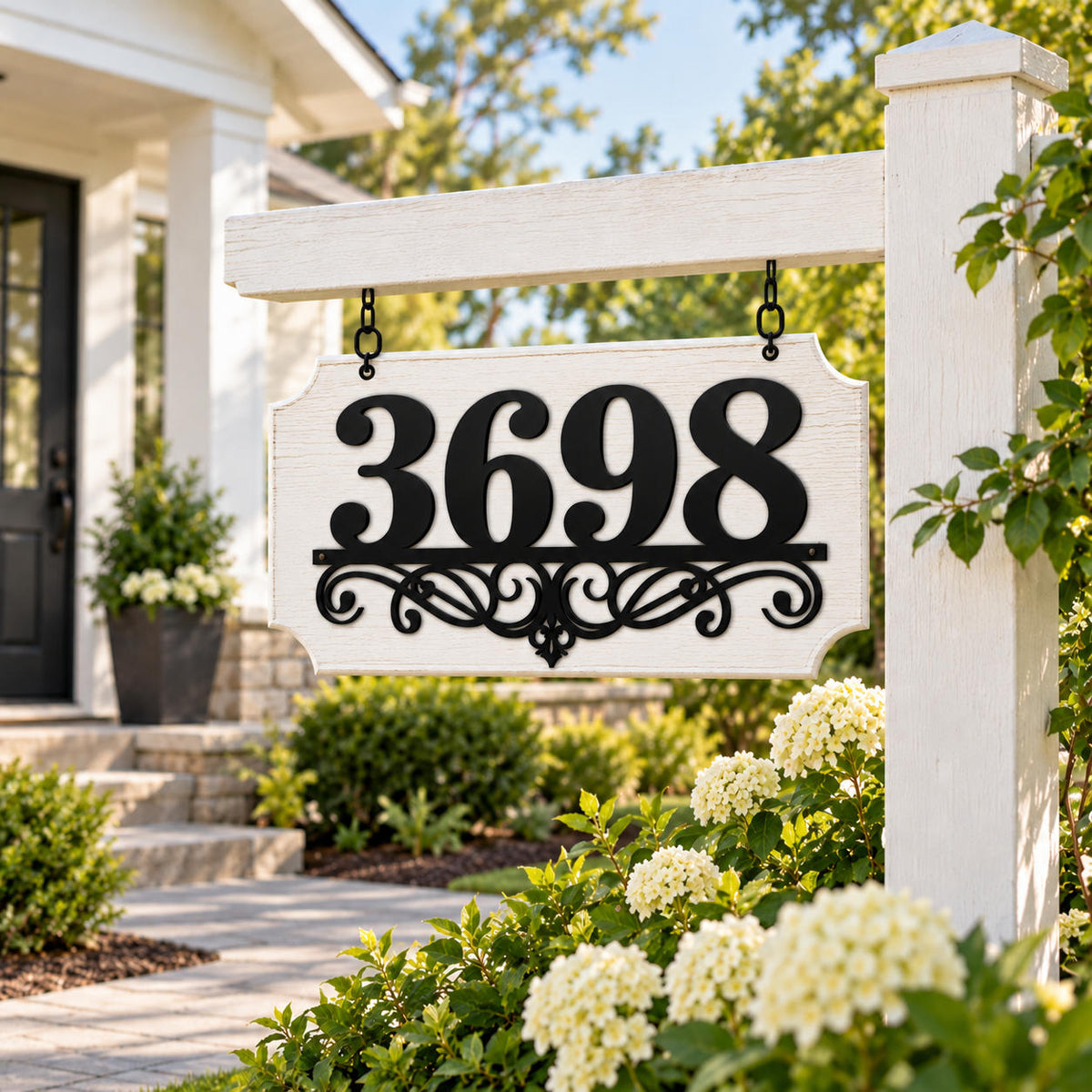 Custom black metal address sign mounted on a white wood backing board and hanging from a garden post.