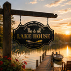 Custom Lake House metal sign with hanging loops suspended by chains from a wooden beam beside a peaceful lakeside dock at sunset.