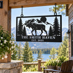 Personalized moose metal sign hanging from chains on a rustic cabin porch overlooking a mountain lake.