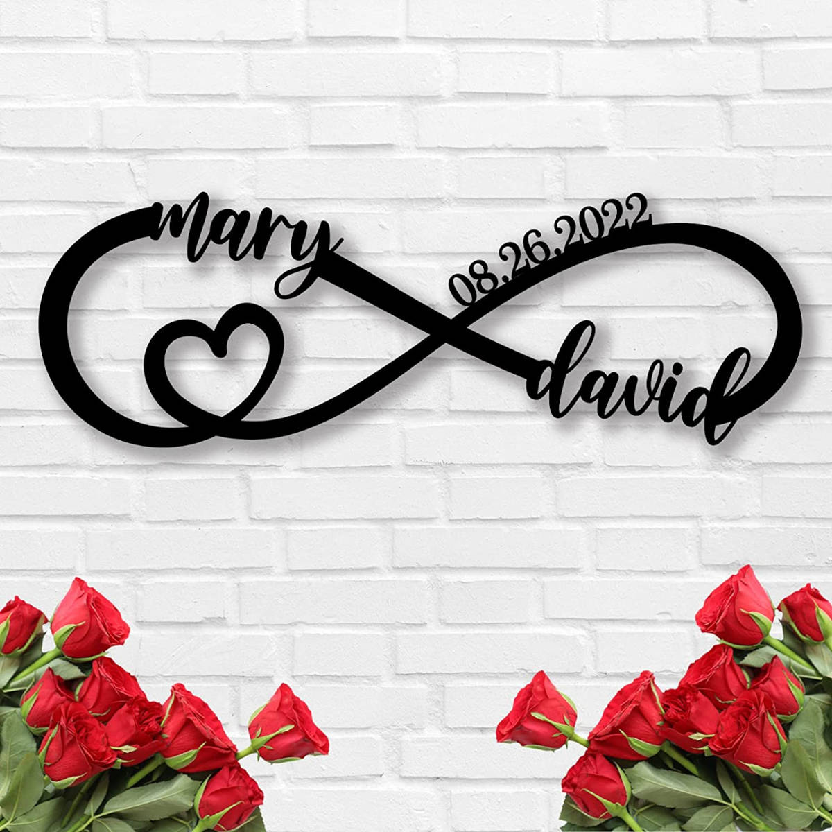 Personalized infinity heart metal sign with custom names and date, laser-cut from black powder-coated steel, displayed against a white brick wall. Main image
