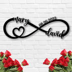 Personalized infinity heart metal sign with custom names and date, laser-cut from black powder-coated steel, displayed against a white brick wall.