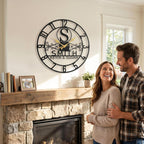 Personalized black steel wall clock with Arabic numerals, gold hands, and custom family names.