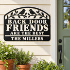 Personalized black metal welcome sign mounted beside a sage green back door with potted plants below.