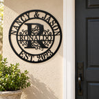 Black metal Ronaldo family monogram sign mounted on a beige stucco wall beside a charcoal front door and potted shrub.