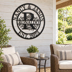 Black metal family monogram sign on a whitewashed wood wall above wicker chairs in a covered patio seating area.