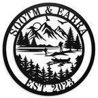 Personalized round black metal lake house sign featuring a custom family name, mountains, pine trees, hikers and canoe design.