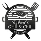 Customized metal BBQ grill name sign featuring a laser-cut steak and grill design, personalized with "Robert's Grill & Chill" and "Est. 2022" on a white brick wall.
