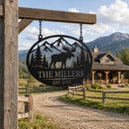 Personalized moose metal family sign hanging at a rustic ranch entrance with mountains in the background.
