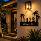 Personalized tropical palm tree metal address sign illuminated by warm porch lighting at night.