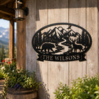 Personalized black metal wilderness family sign with bear, deer, mountains and custom last name displayed on a rustic cabin wall.