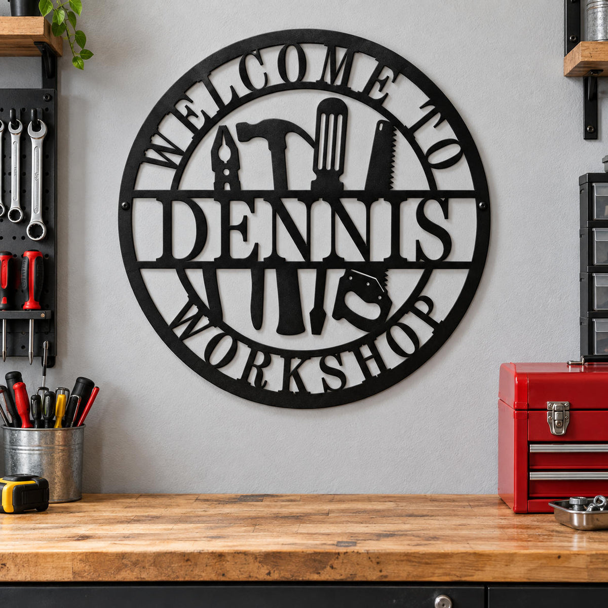 Personalized Dennis workshop metal sign on a gray garage wall above a wooden workbench beside tools and a red toolbox.