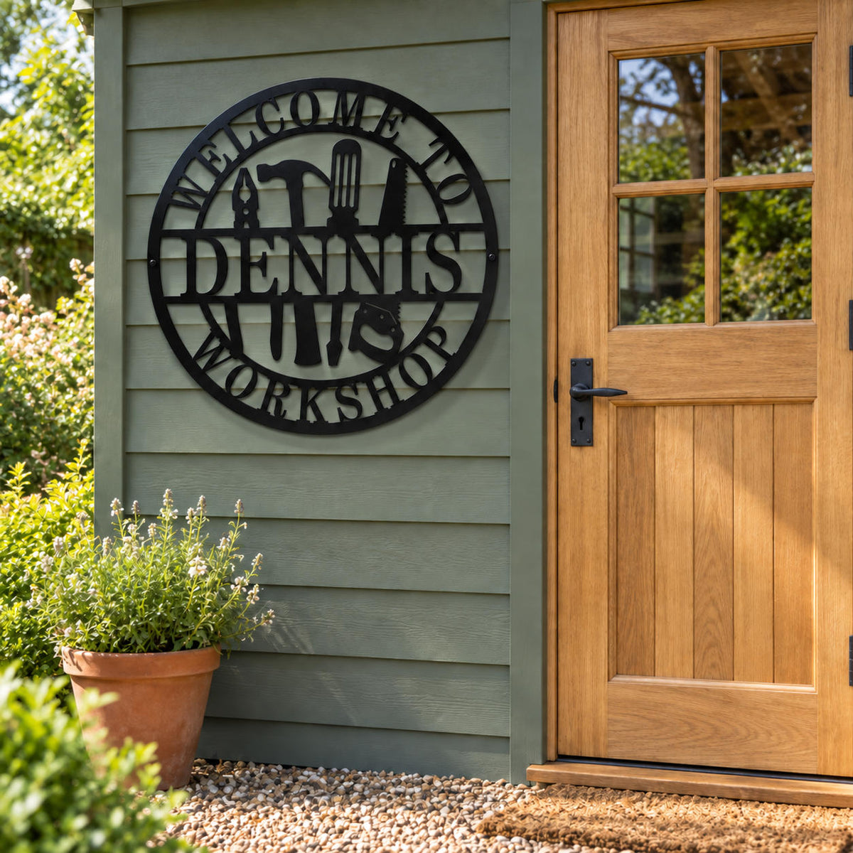Personalized Dennis workshop sign mounted beside an oak door on the sage green siding of a garden workshop.