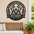 Black metal golden retriever memorial sign for Buddy on a beige covered porch wall above a wooden bench beside a potted fern.