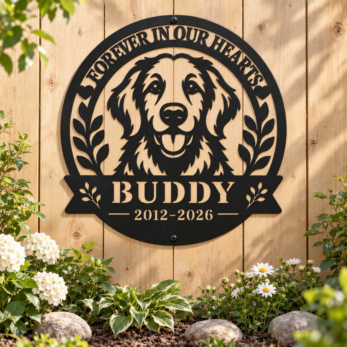 Black metal golden retriever memorial sign for Buddy mounted on a wooden garden fence above white flowers, greenery, and natural stones.
