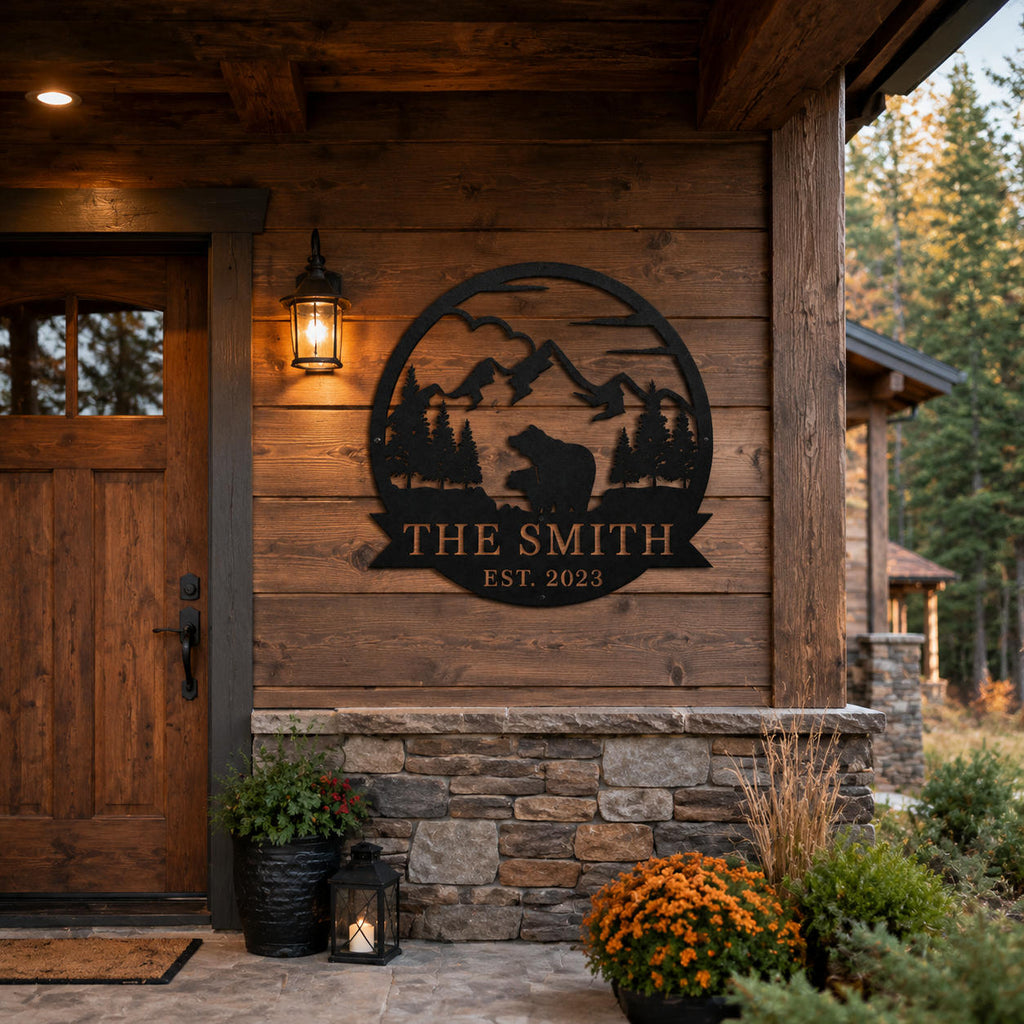 Custom black metal family sign installed on a rustic cabin entrance wall with mountain forest background