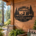 Black deer family metal sign mounted on a rustic woodland cabin wall surrounded by pine trees